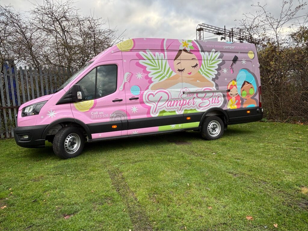 Pink Essex Pamper Bus with colourful illustrations, parked on grass